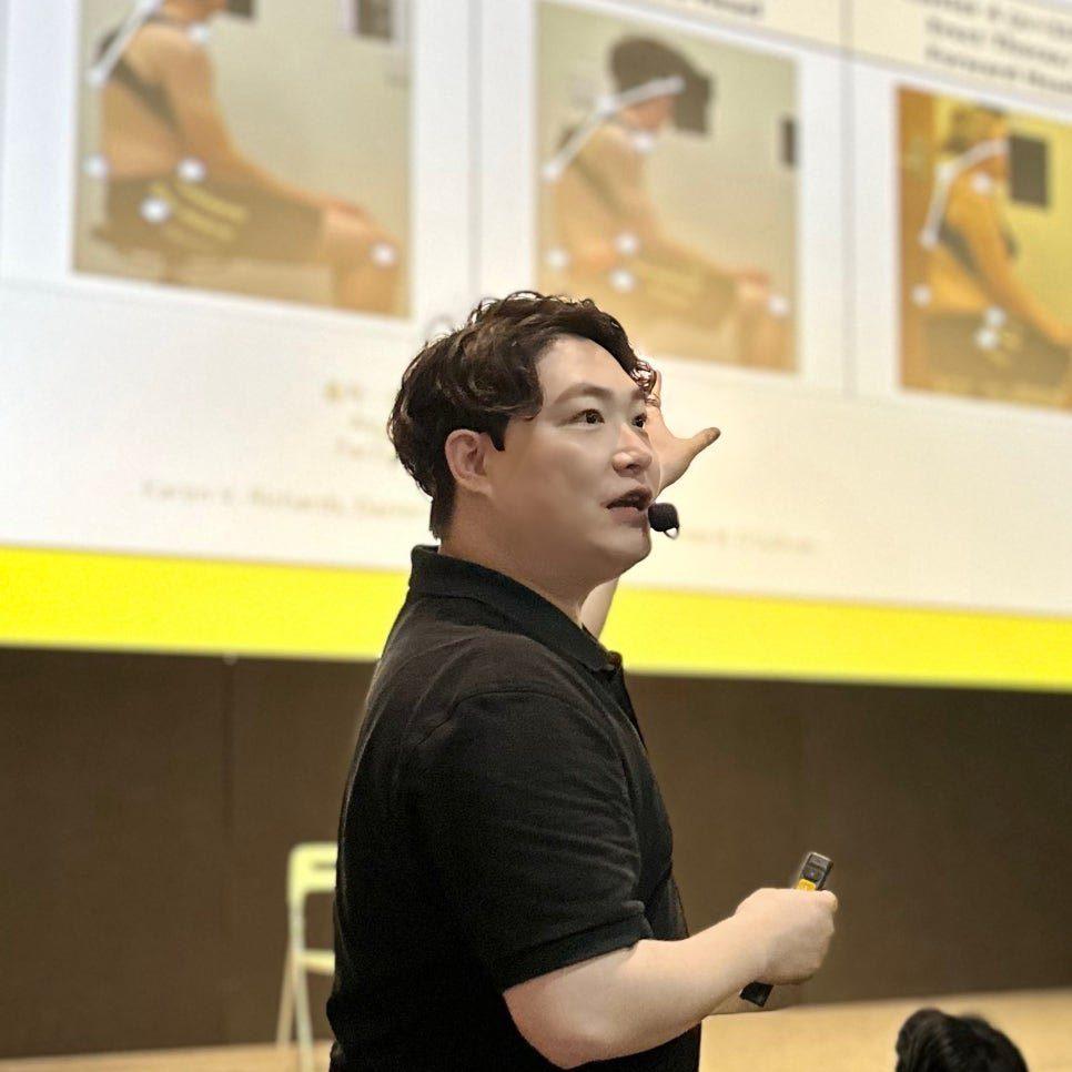 검은 셔츠에 마이크를 차고 슬라이드를 가리키며 설명하는 물리치료사 김윤하