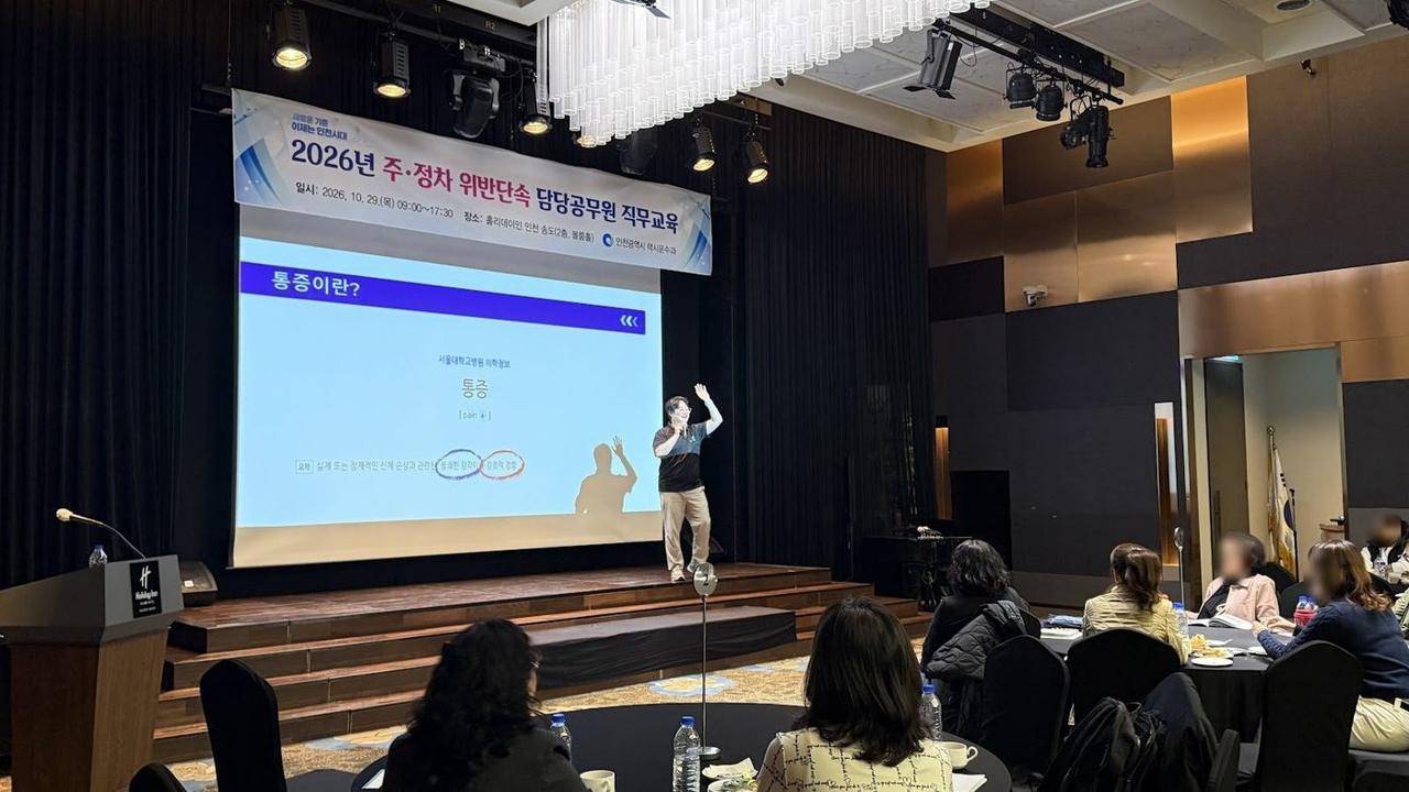 호텔 연회장 무대에서 슬라이드를 띄우고 팔을 들어 설명하는 김윤하와 객석의 참가자들